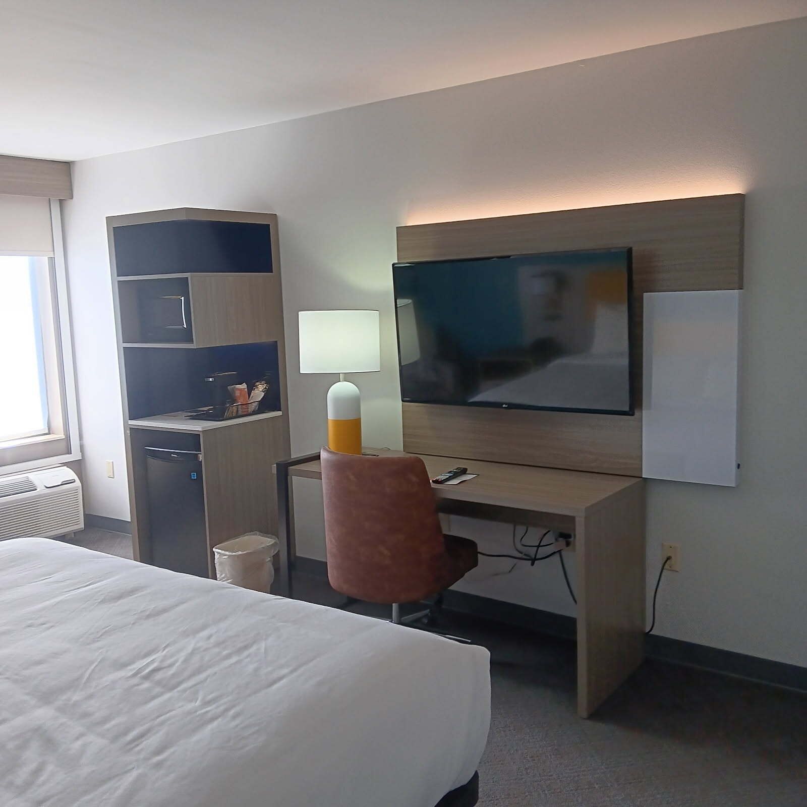 Une chambre d’hôtel équipée d’un lit, d’un bureau, d’une chaise, d’une télévision et d’une petite kitchenette.
