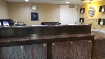 A reception desk with a clock, a sign for Comfort Inn, and a security camera on the ceiling.