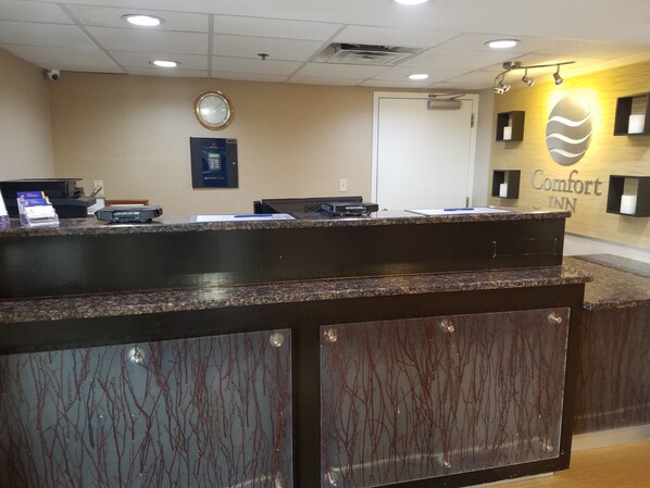 A reception desk with a clock, a sign for Comfort Inn, and a security camera on the ceiling.