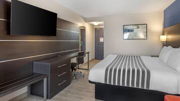 Une chambre d’hôtel moderne avec un grand lit, un bureau avec une chaise, un téléviseur à écran plat et un tableau au mur.
