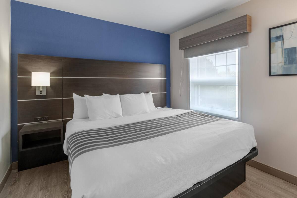 Ein modernes Hotelzimmer mit einem großen Bett, einem Nachttisch, einer Wandlampe und einem Fenster mit Blick.