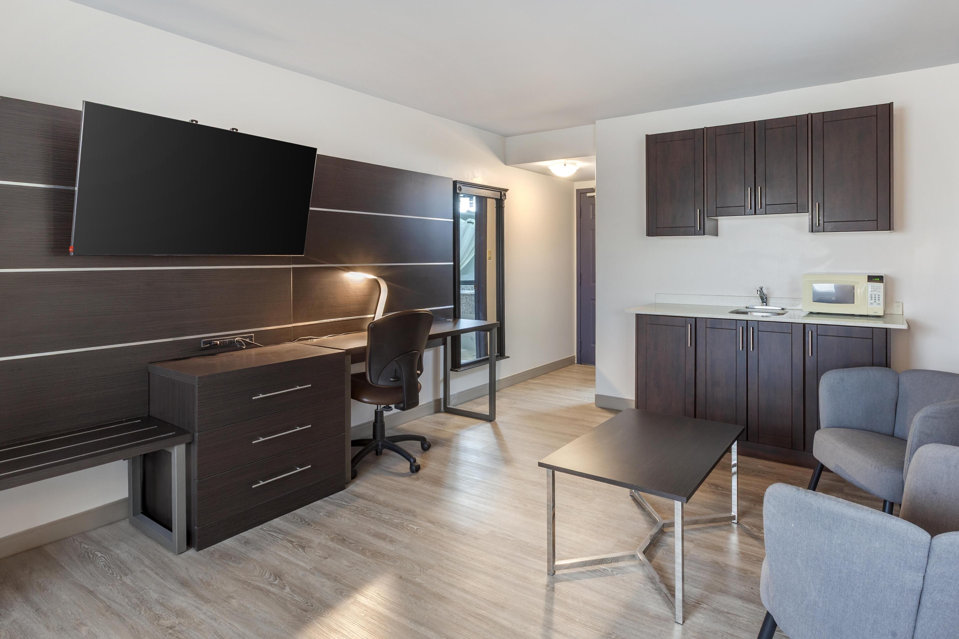 A modern kitchen with dark cabinets, a microwave, and a flat-screen TV mounted above the counter.