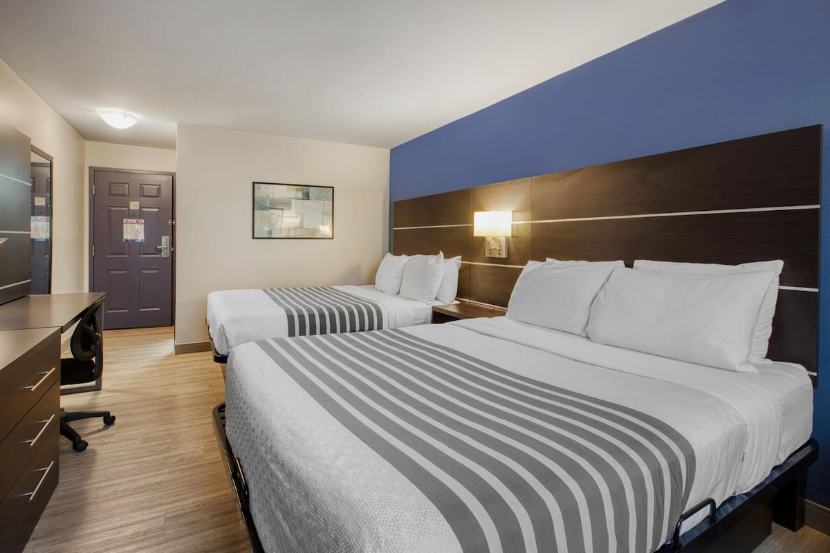 Ein Hotelzimmer mit zwei Betten, einem Schreibtisch, einem Stuhl, einem Nachttisch und einer Wandlampe.