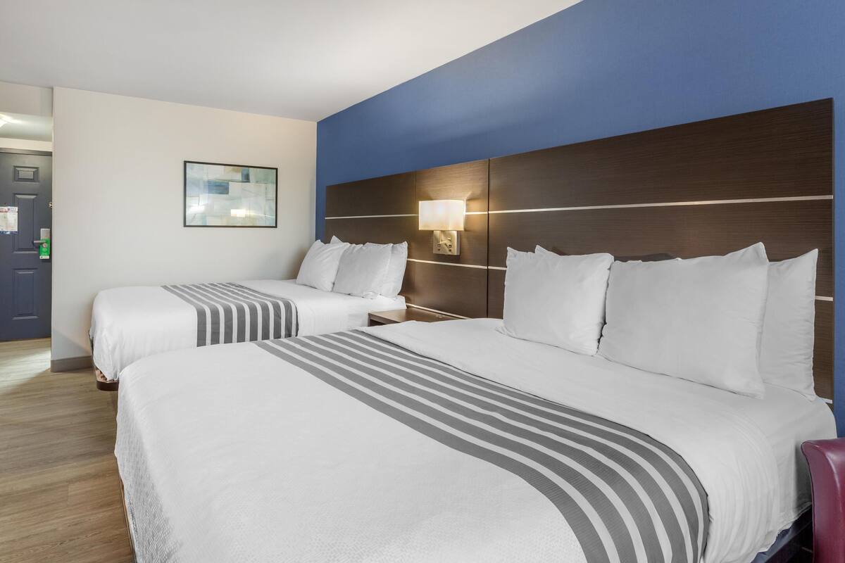 Ein Hotelzimmer mit zwei Betten, einem Nachttisch, einer Wandlampe und einem gerahmten Bild an der Wand.