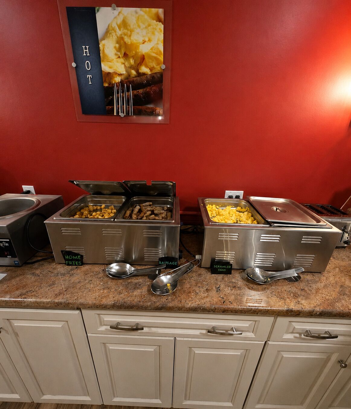A buffet setup with labeled containers for home fries, sausage, scrambled eggs, and a hot dish.