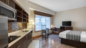 Une chambre d’hôtel de taille réduite, équipée d’une kitchenette, d’un lit, d’un bureau et d’une télévision.