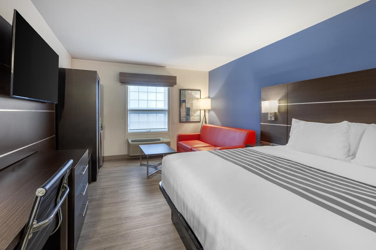 Ein Hotelzimmer mit Bett, Schreibtisch, Fernseher, einem roten Sofa und einem Fenster.