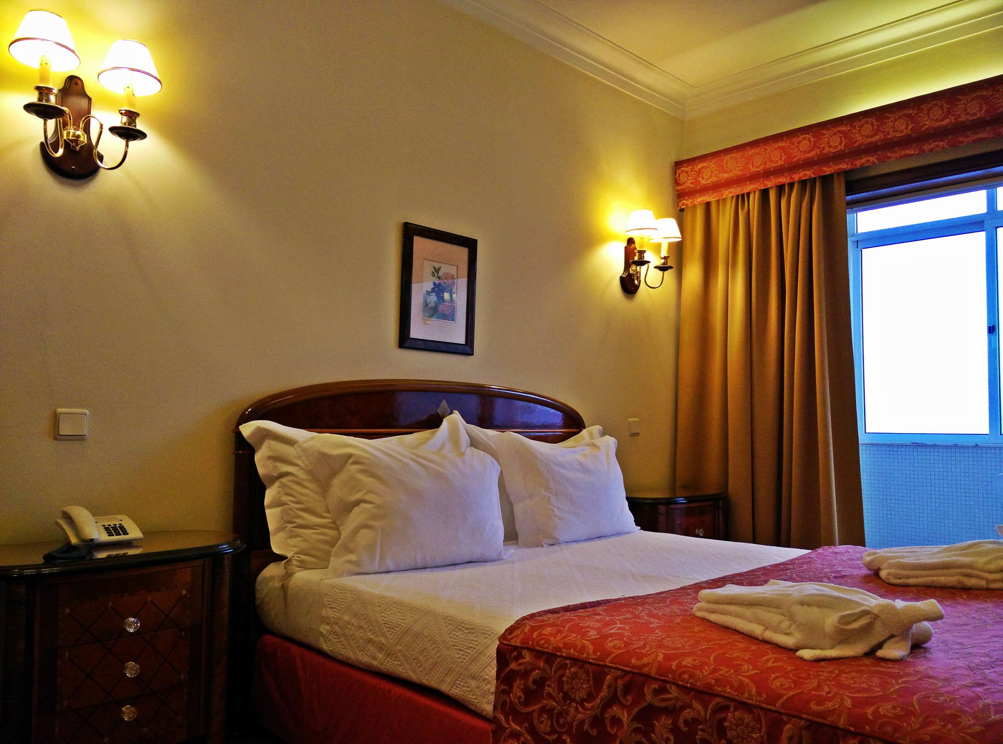 Habitación de hotel con una cama grande, dos lámparas de noche, un teléfono y una ventana con cortinas.