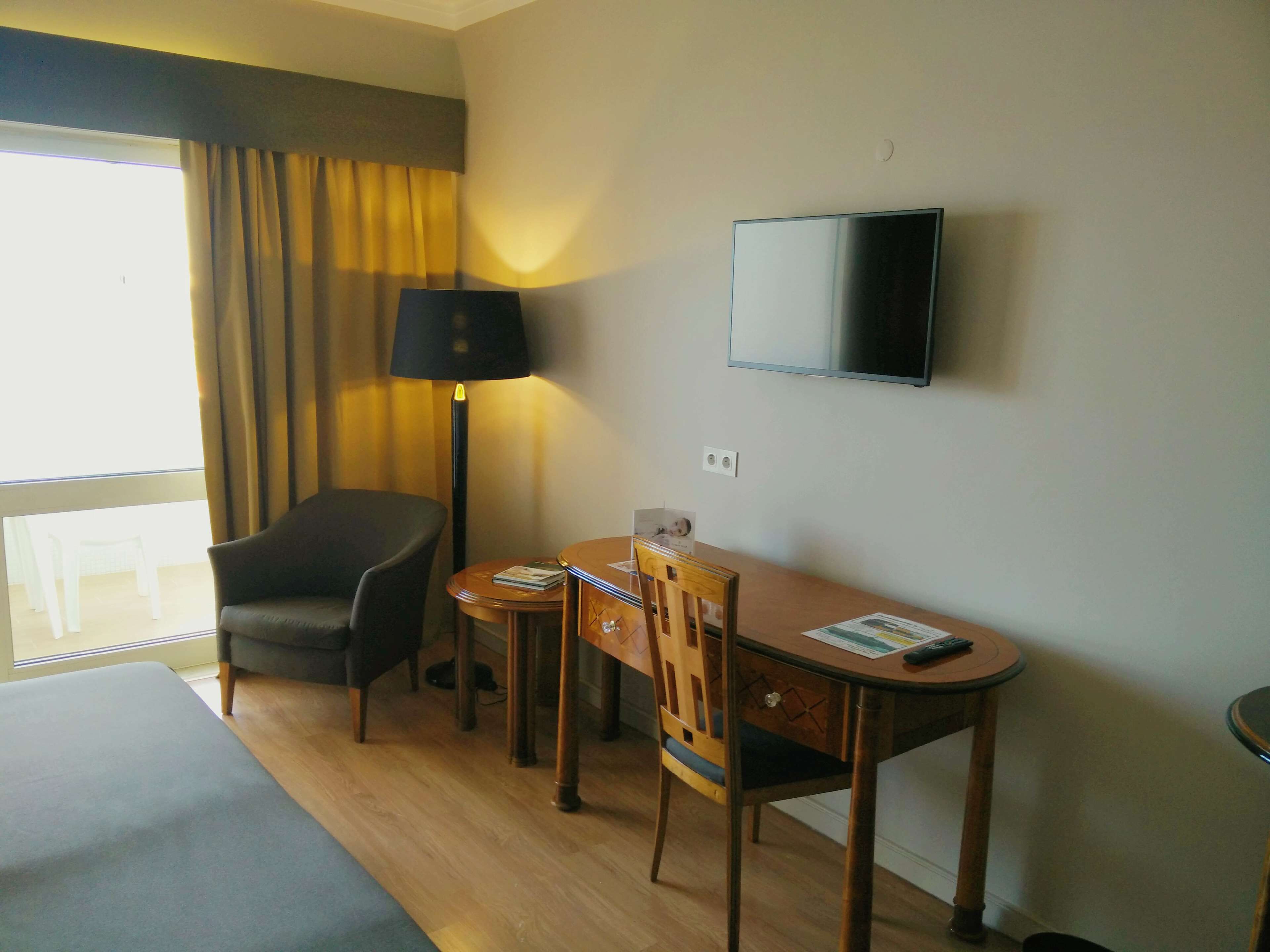 Et hotelværelse med en seng, et skrivebord med stol, en lampe og et fjernsyn på væggen.