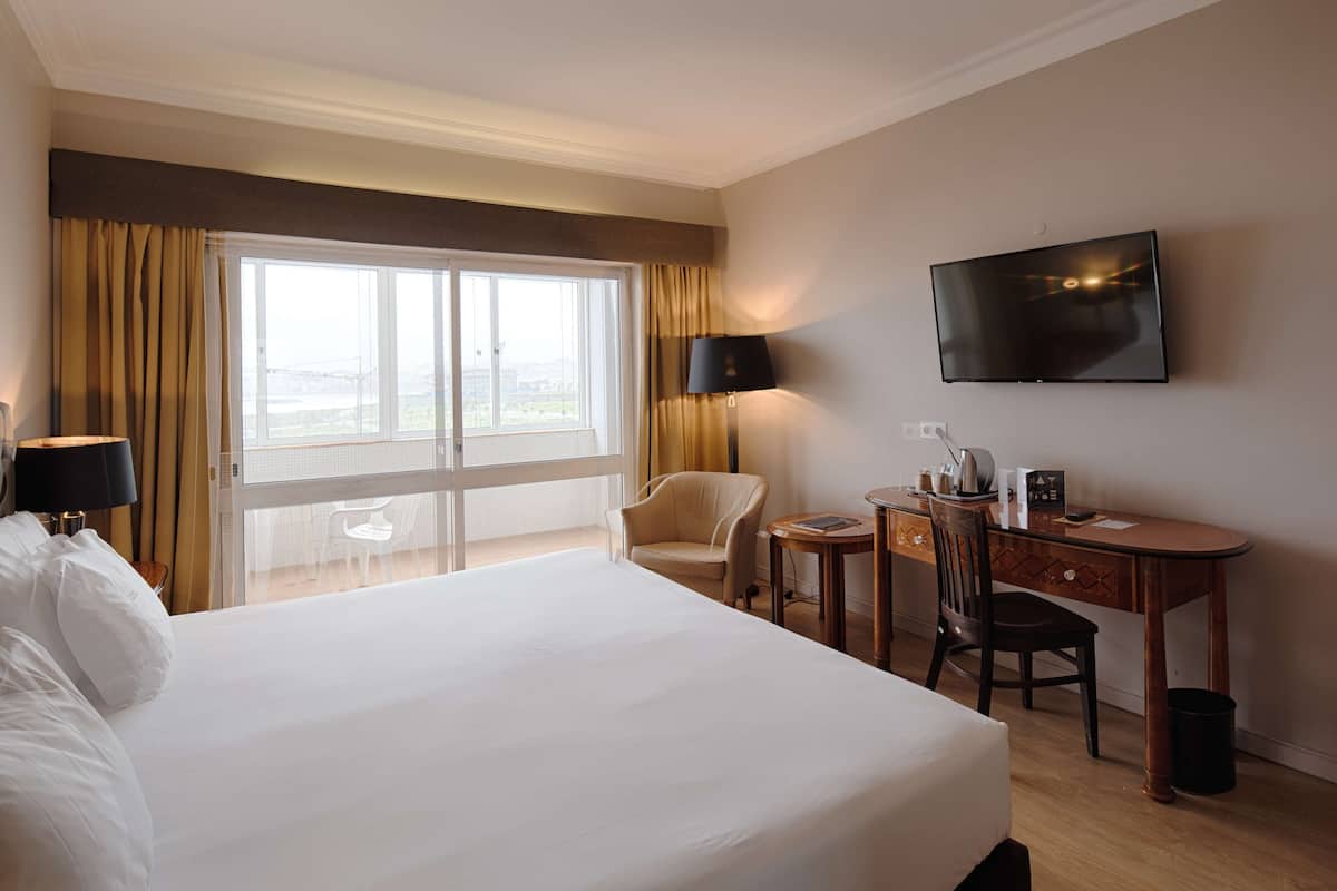 Une chambre d’hôtel avec un grand lit, un bureau avec une chaise, une télévision et une vue sur la ville par la fenêtre.