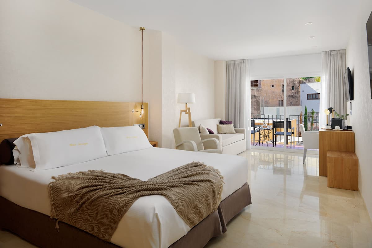 Hotelkamer met een groot bed, een bureau, een stoel en een balkon met uitzicht op gebouwen.