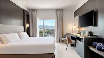 Habitación de hotel con una cama grande, un escritorio, una silla, un televisor y vistas a la ciudad.