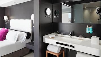 Ein modernes Hotelzimmer mit einem großen Bett, einem weißen Schminktisch mit Spiegel und zwei hölzernen Hocker mit Handtüchern.