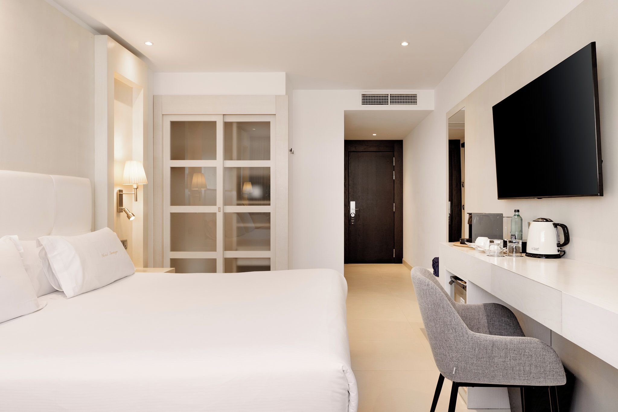 Una habitación de hotel con una cama, un escritorio, una silla, un televisor y una cafetera.