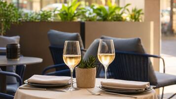 Un área de comedor al aire libre con dos mesas, cada una dispuesta con platos, cubiertos y copas de vino blanco.