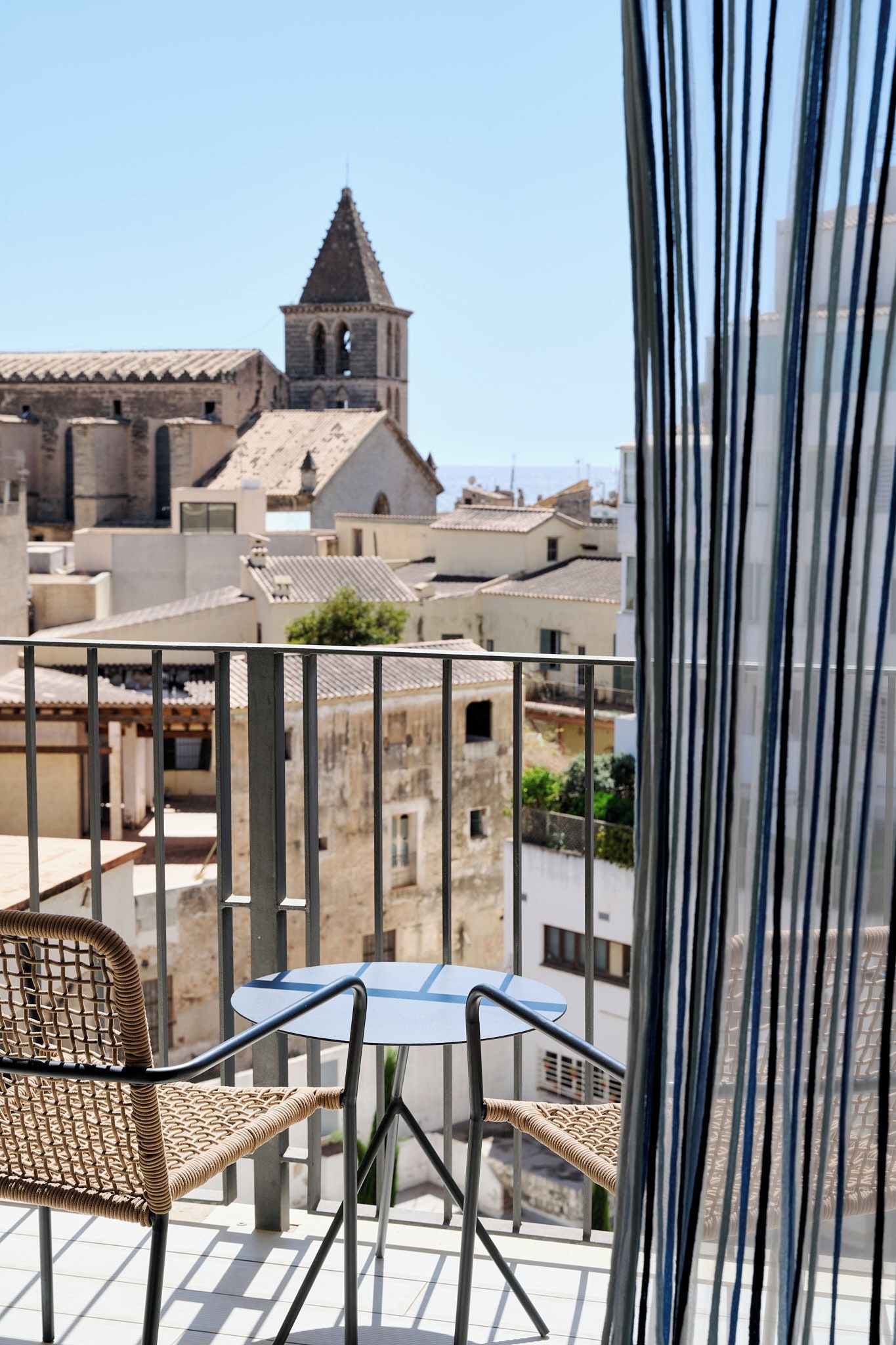 A balcony with a table and chairs, overlooking a historic town with a church tower.