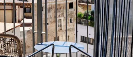 A balcony with a table and chairs, overlooking a historic town with a church tower.