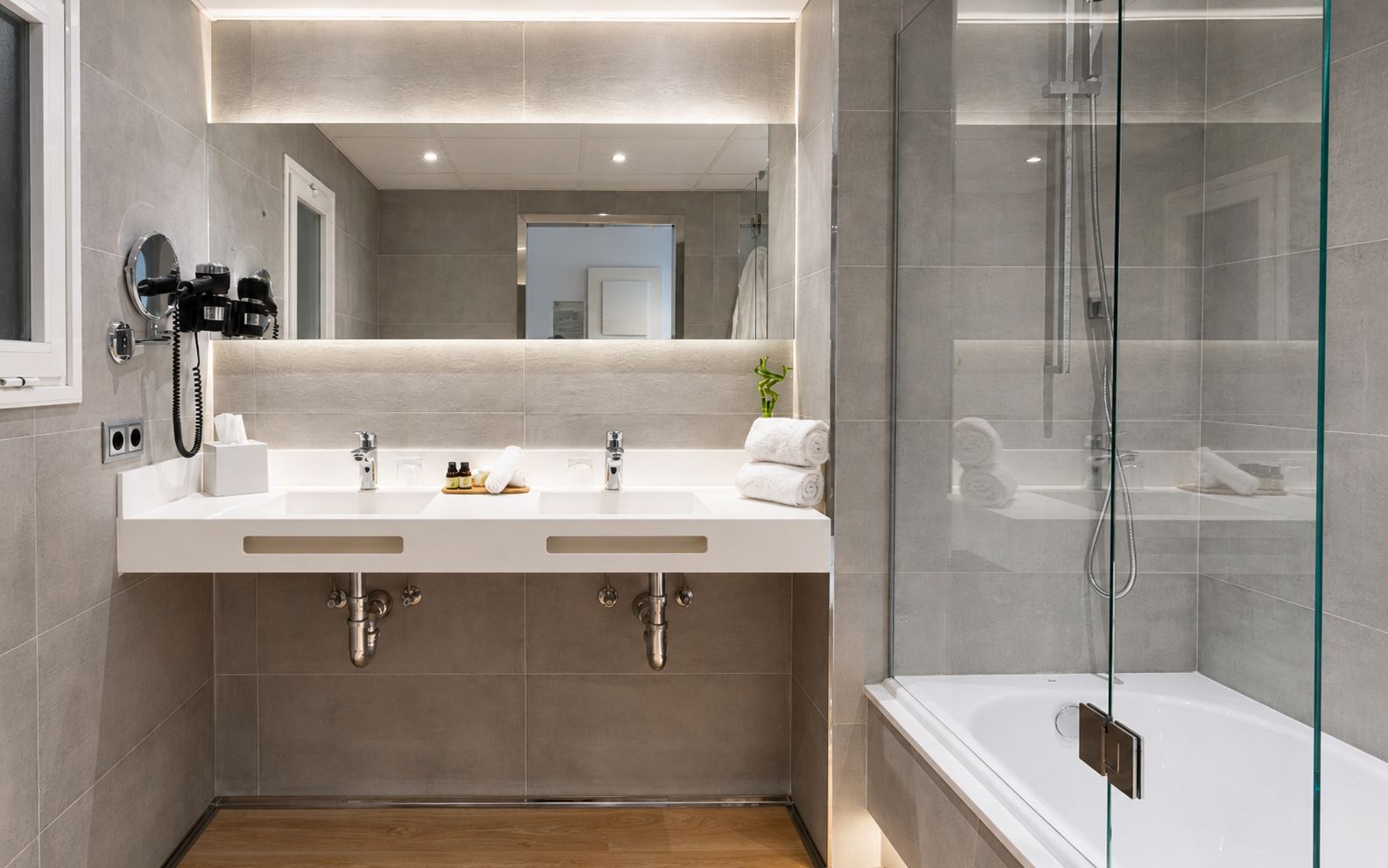 Un baño moderno con dos lavamanos, una cabina de ducha con mampara de vidrio y piso de madera.