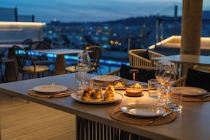 A dining table set with plates, glasses, and cutlery, overlooking a cityscape at dusk. - Hotel Saratoga (Palma de Mallorca)