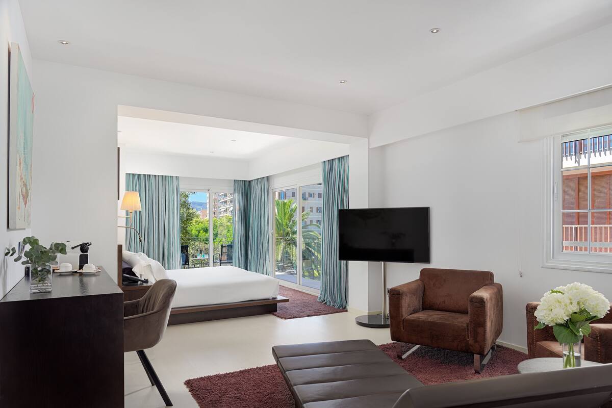 Een moderne hotelkamer met een bed, een televisie, een bruine leren fauteuil, een bureau met een lamp en uitzicht op de omgeving.