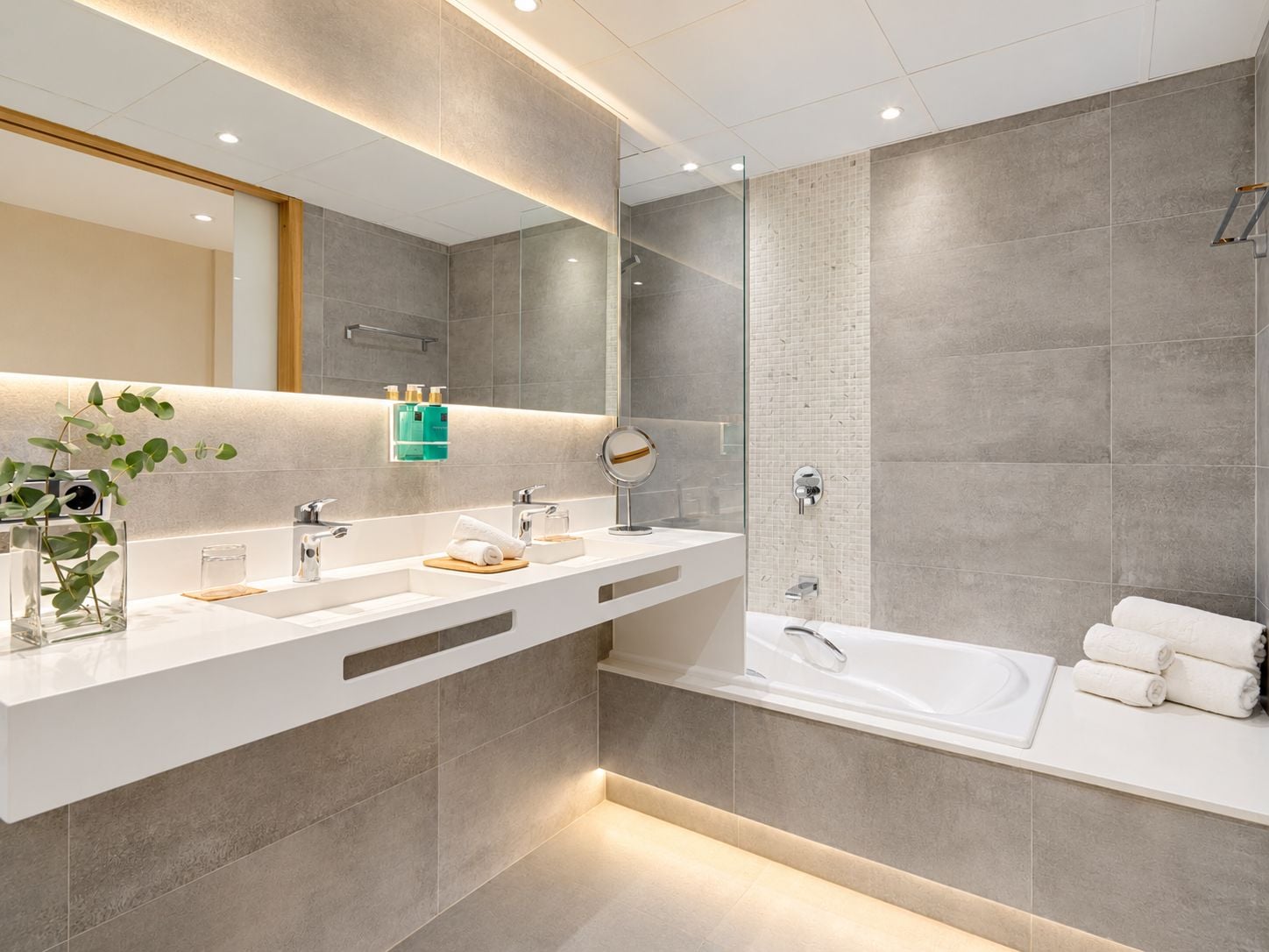 Un baño moderno con un espejo grande, dos lavamanos, una ducha y cabina de ducha con paredes de vidrio.