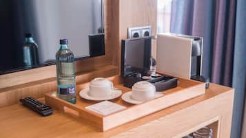 Habitación de hotel con un escritorio de madera, una botella de agua, dos tazas blancas, un control remoto, una cafetera y una bandeja.