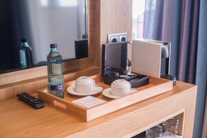 Habitación de hotel con un escritorio de madera, una botella de agua, dos tazas blancas, un control remoto, una cafetera y una bandeja.