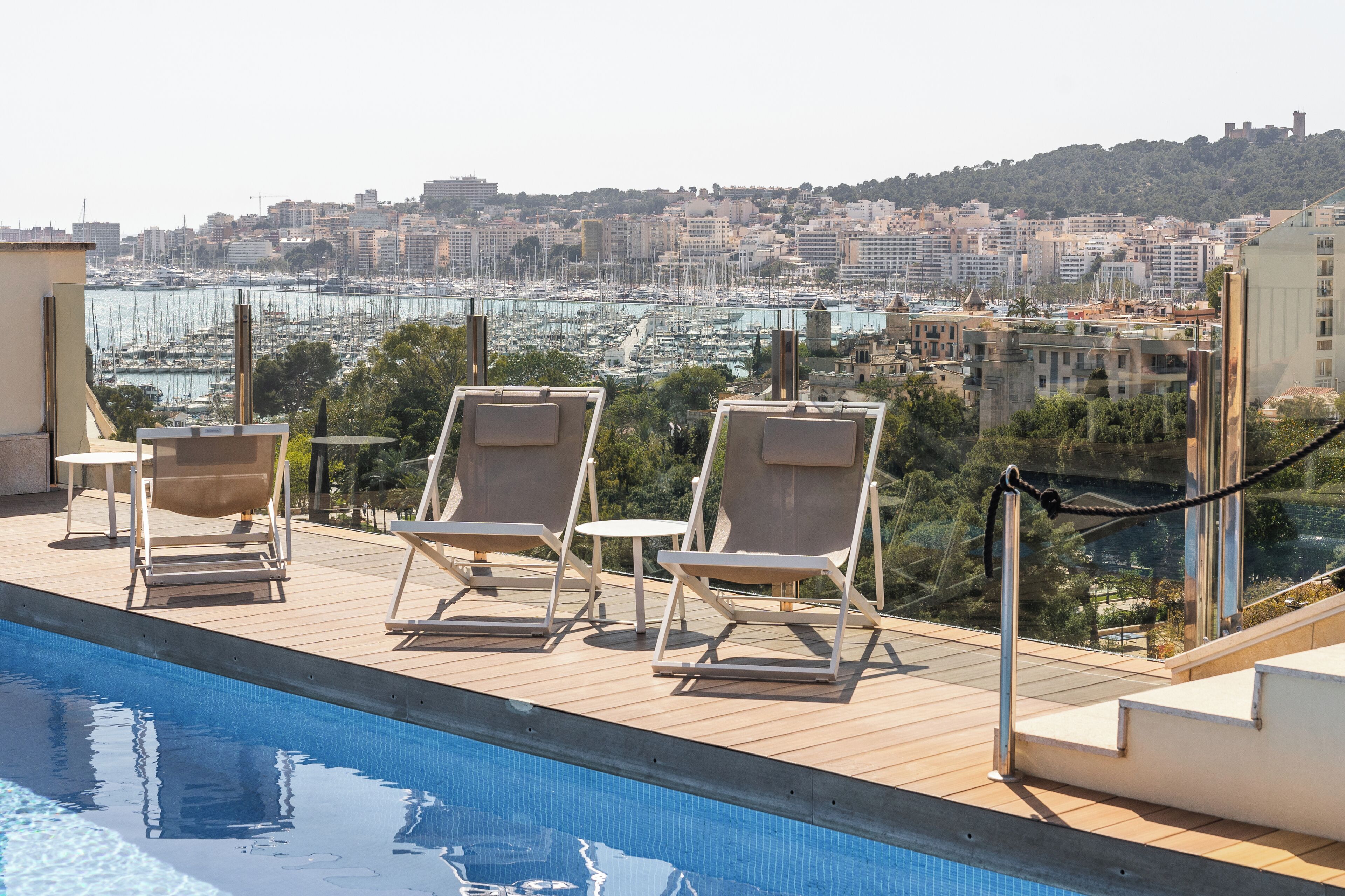A rooftop pool area with lounge chairs and a view of a marina and cityscape.
