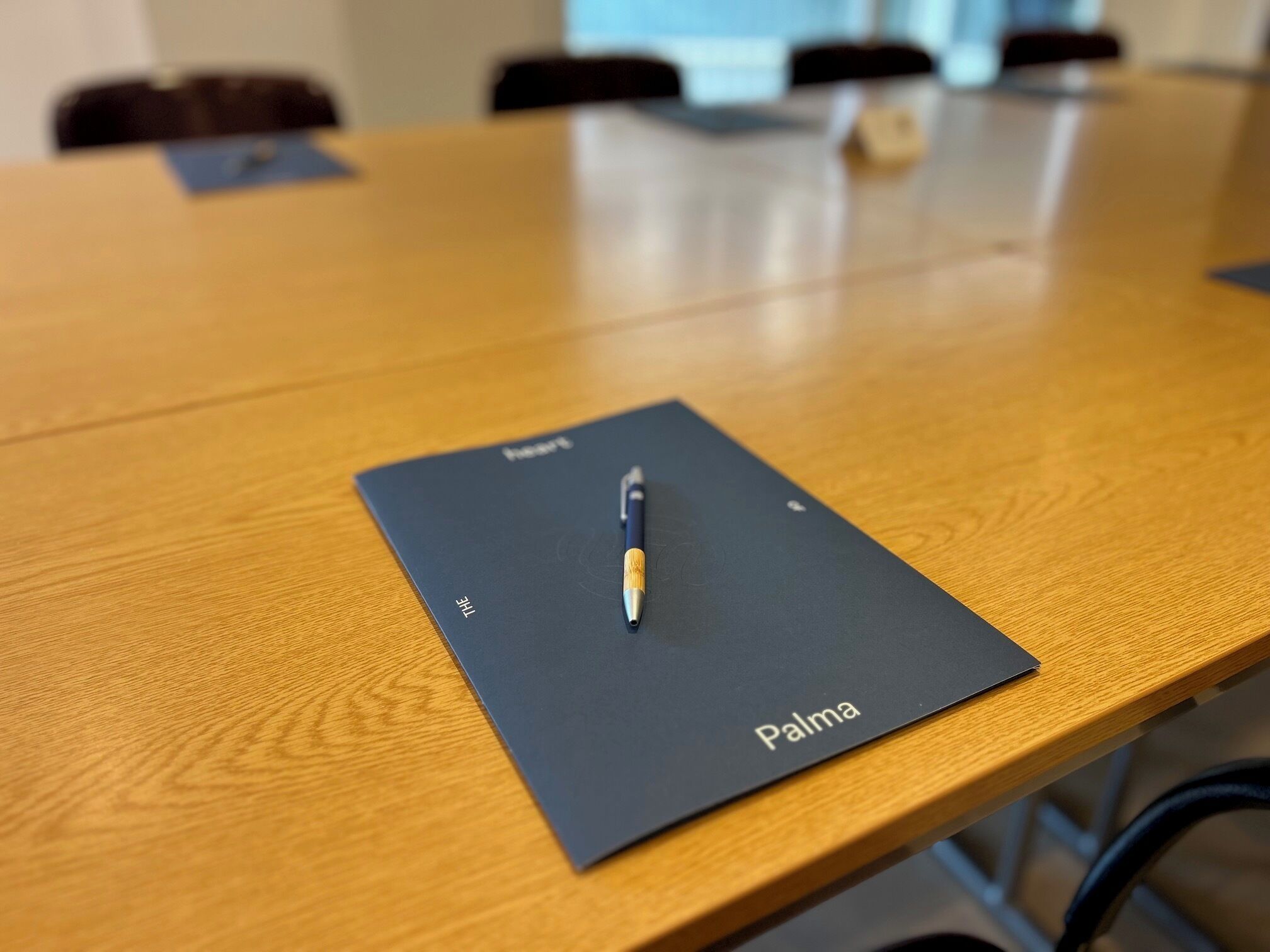 Une table de conférence sur laquelle se trouve un dossier noir portant l’inscription « Palma » et un stylo.