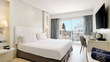 Una habitación de hotel con una cama grande, un escritorio, una silla, un televisor de pantalla plana y un balcón con vistas a edificios.