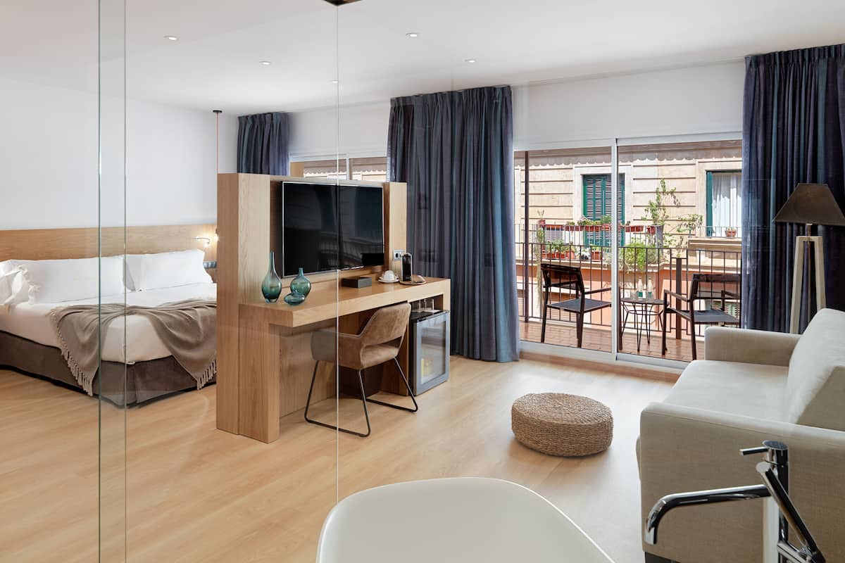 Een hotelkamer met een bed, een bureau met een televisie, een balkon met een tafel en stoelen, en een bank.