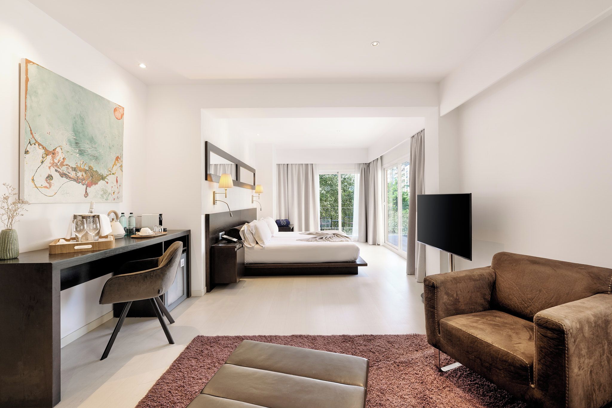 A modern hotel room with a bed, a desk, a chair, a TV, and a large window.