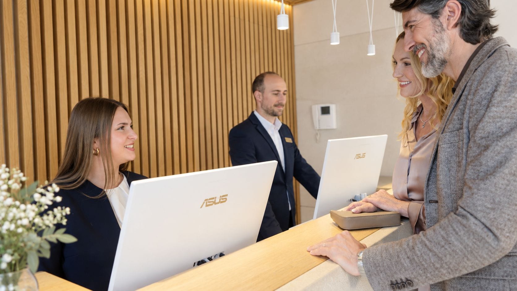 A reception desk with three ASUS laptops, a wooden panel wall, and a modern light fixture.