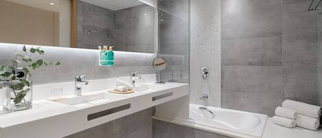 A modern bathroom with a large mirror, two sinks, a bathtub, and a shower.