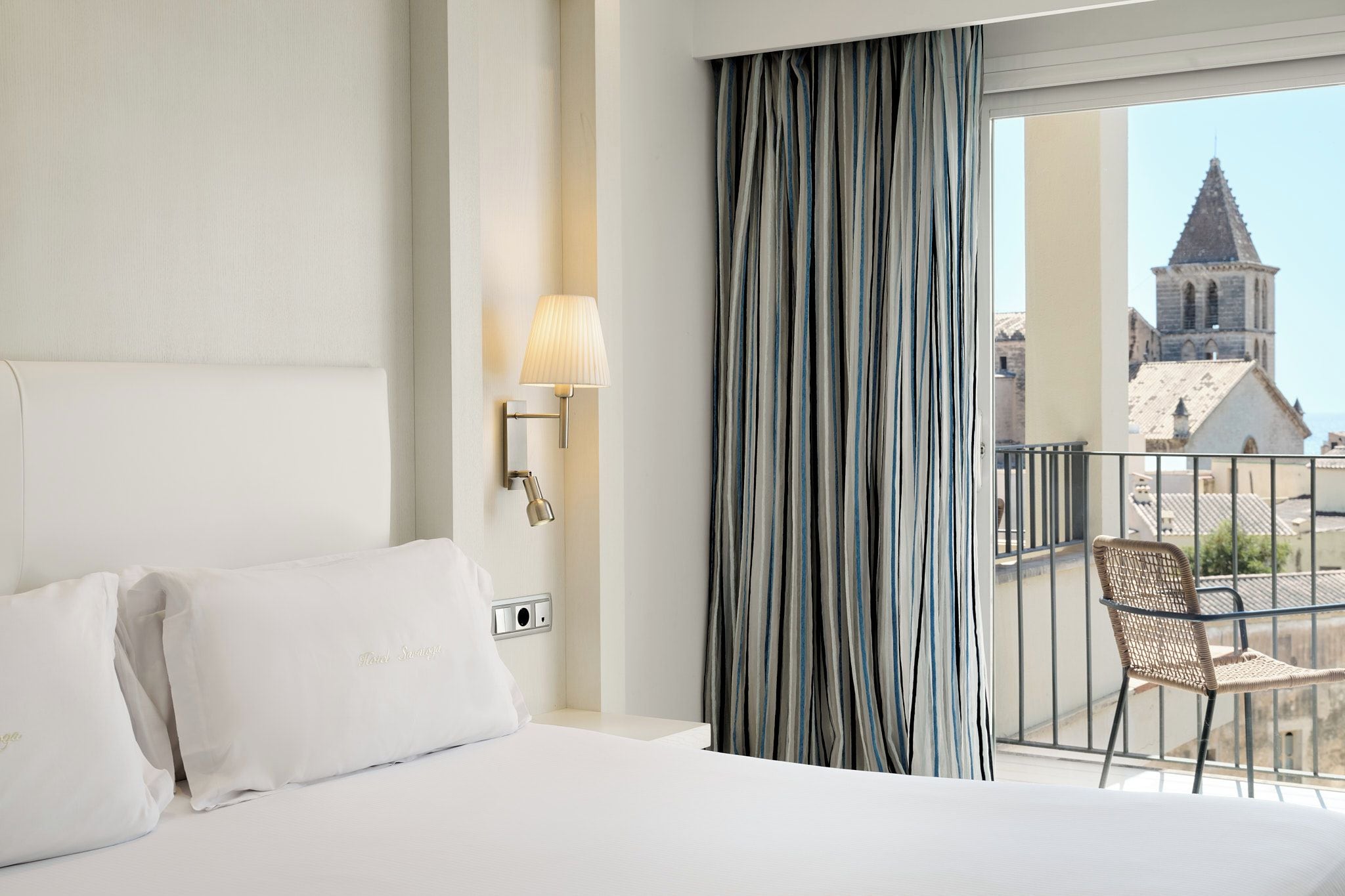 Een hotelkamer met een bed, een lamp, een raam met gordijnen en uitzicht op een gebouw.