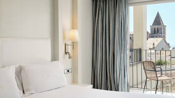 Una habitación de hotel con cama, lámpara, ventana con cortinas y vista a un edificio.