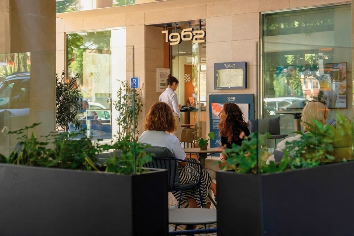 An outdoor seating area with tables and chairs, a glass wall, and a sign indicating the year 1962.