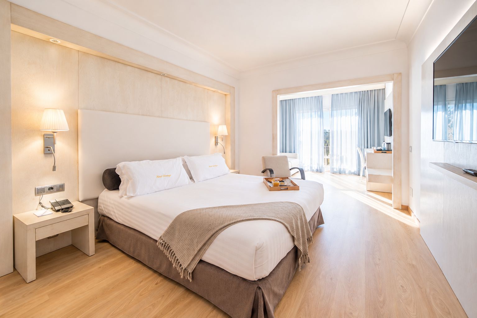 Una habitación de hotel con una cama grande, mesitas de noche, un escritorio y vistas al exterior.