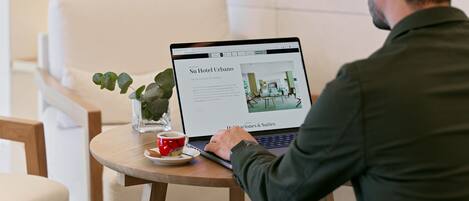 A person using a laptop at a wooden table with a red cup and saucer.