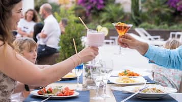 A dining table with various dishes and drinks, surrounded by people.