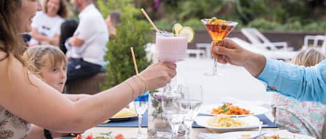 Una mesa de comedor con diversos platos y bebidas, rodeada de gente.