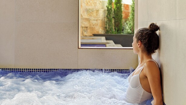 Une femme dans un jacuzzi, avec vue sur un bâtiment et la verdure environnante.