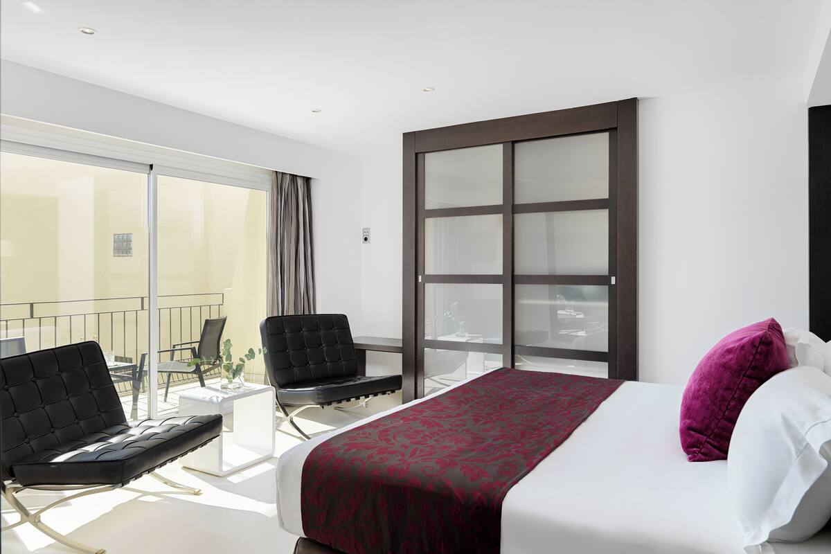 Een moderne hotelkamer met een groot bed, een zwarte leren fauteuil, een tafeltje en een balkon met een glazen deur.