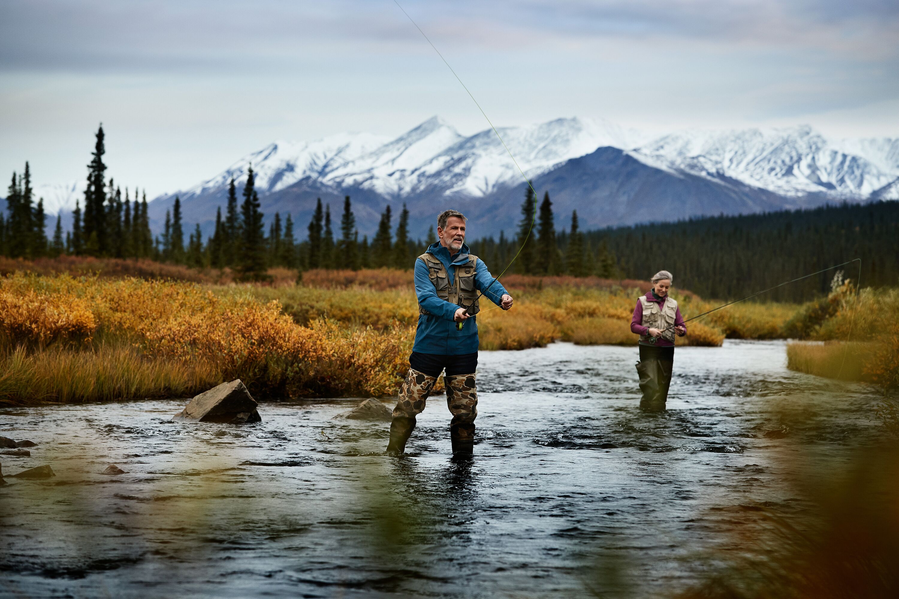Two people standing in a river with mountains in the background.