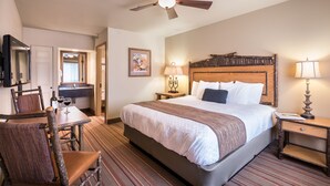 A hotel room with a large bed, a desk with a chair, a ceiling fan, and a TV on the wall. - Denali Princess Wilderness Lodge (Denali National Park)
