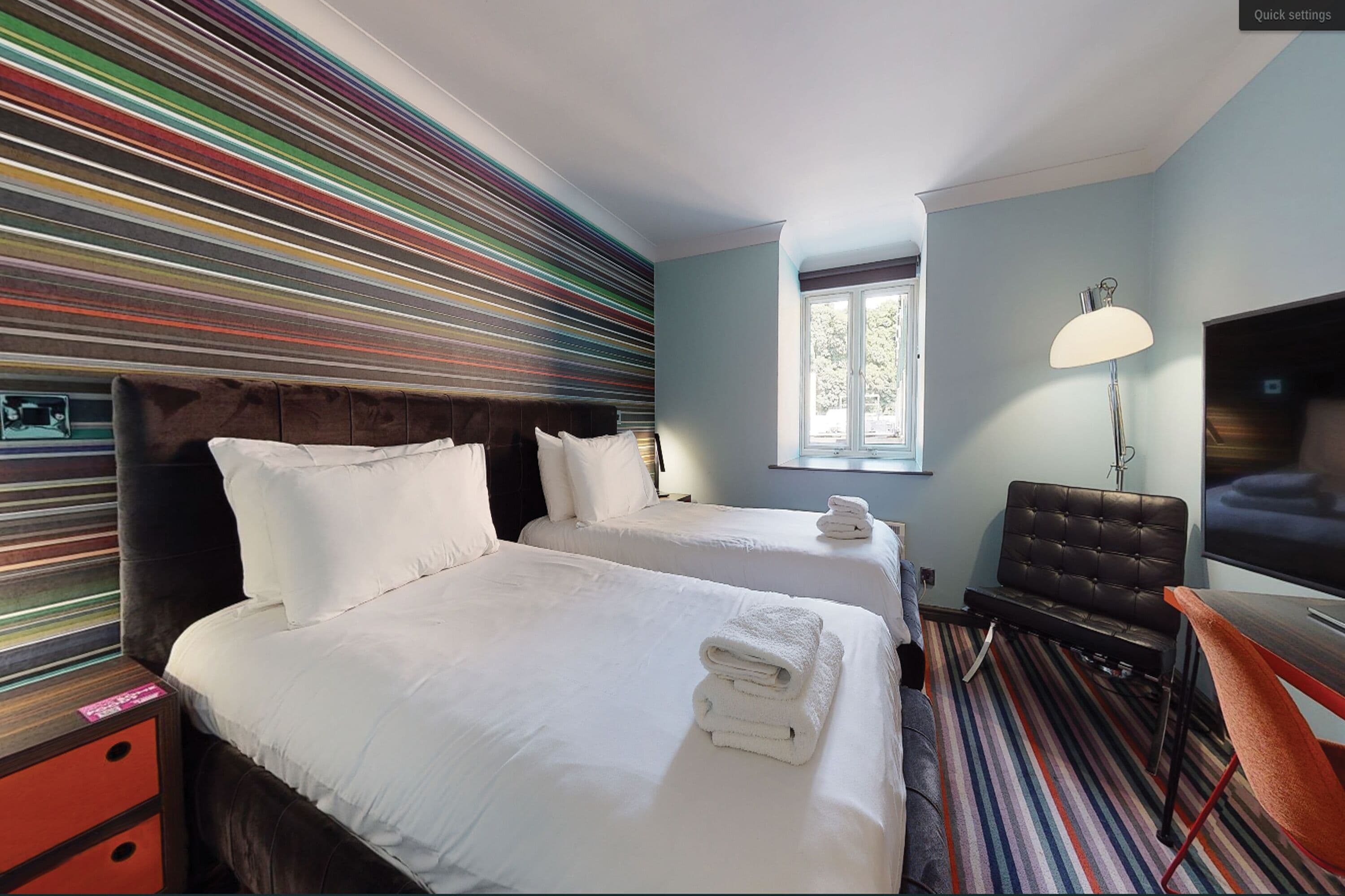 A hotel room with two beds, a TV, a lamp, and a window.