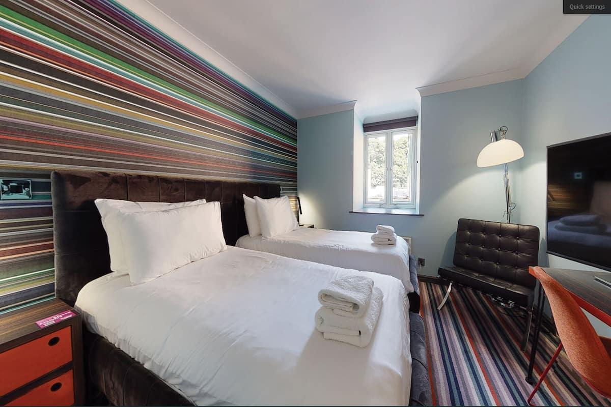 Ein Hotelzimmer mit zwei Betten, einem Fernseher, einer Lampe und einem Fenster.
