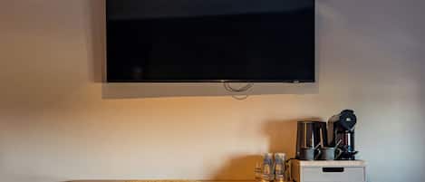 Una TV a schermo piatto montata a parete, una macchina per caffè e un tavolino con una sedia.
