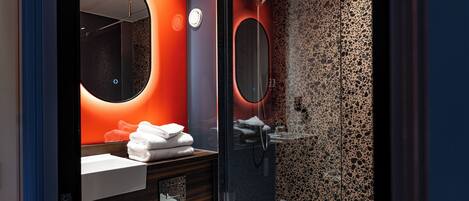 Un baño moderno con cabina de ducha de vidrio, un espejo redondo y un mueble de tocador con lavamanos y toallero.