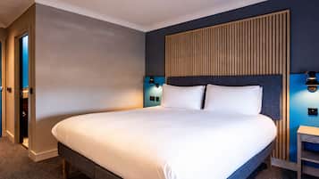 A hotel room with a large bed, a wooden headboard, two bedside lamps, and a small nightstand.